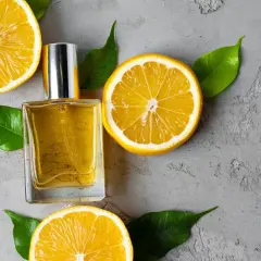 Szklana buteleczka perfum otoczona plasterkami cytryny i zielonymi listkami. Zapach cytrusowy unosi się w powietrzu.