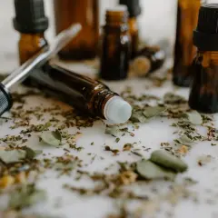 Butelki z ciemnego szkła, pipeta i rollerball otoczone suszonymi ziołami. Wskazują na trwałość perfum oznaczenia.