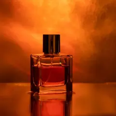 Szklana buteleczka perfum z płynem w odcieniu bursztynu, otoczona ciepłym, świetlistym tłem.
