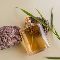 Szklana butelka z płynem, otoczona kamieniami i trawą. Klasyczne perfumy lat 90 męskie, które przywołują wspomnienia.
