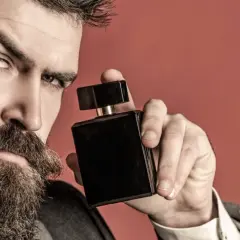 Mężczyzna z brodą trzyma czarny flakon perfum. Zastanawia się, gdzie psikac perfumami, by podkreślić swój styl.