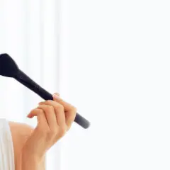 Uśmiechnięta blondynka uczy się, jak nauczyć się malować twarz, nakładając róż puszystym pędzlem.