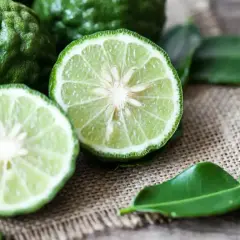 Zielone, pomarszczone owoce i przekrojone na pół limonki, z liśćmi na płótnie. Czuć, jak pachnie bergamotka.
