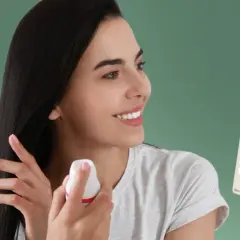 Szukasz co zamiast suchego szamponu? Kobieta aplikuje odświeżający spray na włosy, obok stoją różne marki suchych szamponów.
