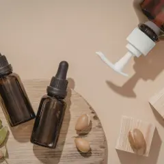 Butelki z ciemnego szkła z pipetami i pompką, obok orzechy arganowe i liście. Naturalny olej arganowy na włosy.