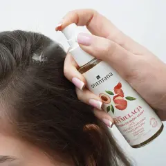 Dłoń aplikuje spray na skórę głowy, by pobudzić skręty włosów. Produkt zawiera liczi i argininę.