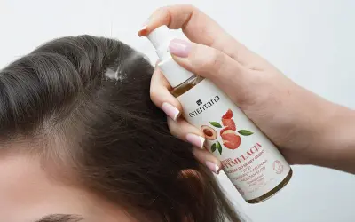 Dłoń aplikuje spray na skórę głowy, by pobudzić skręty włosów. Produkt zawiera liczi i argininę.