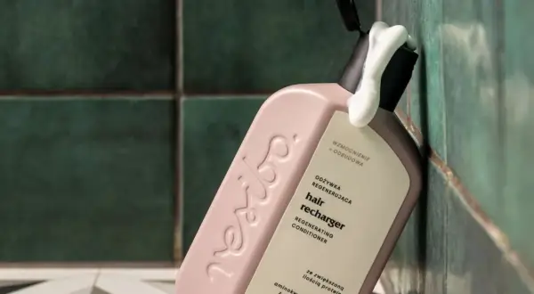 Omo jakie odżywki! Różowa butelka regenerującej odżywki do włosów "hair recharger" z pianką wydobywającą się z otwartego dozownika, na tle zielonych, łazienkowych płytek.