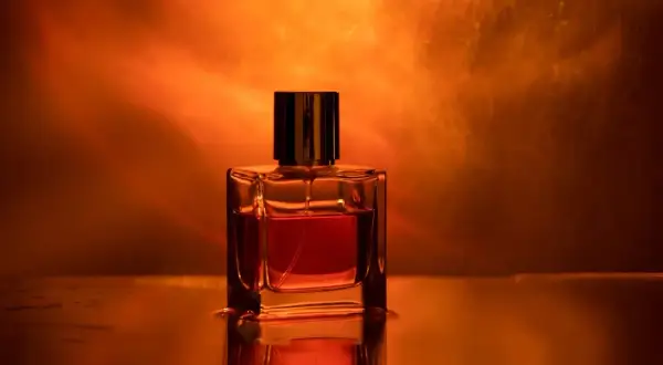 Szklana buteleczka perfum z płynem w odcieniu bursztynu, otoczona ciepłym, świetlistym tłem.