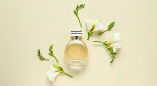Elegancka butelka perfum otoczona delikatnymi kwiatami frezji. Zapach frezji unosi się w powietrzu, tworząc subtelną kompozycję.