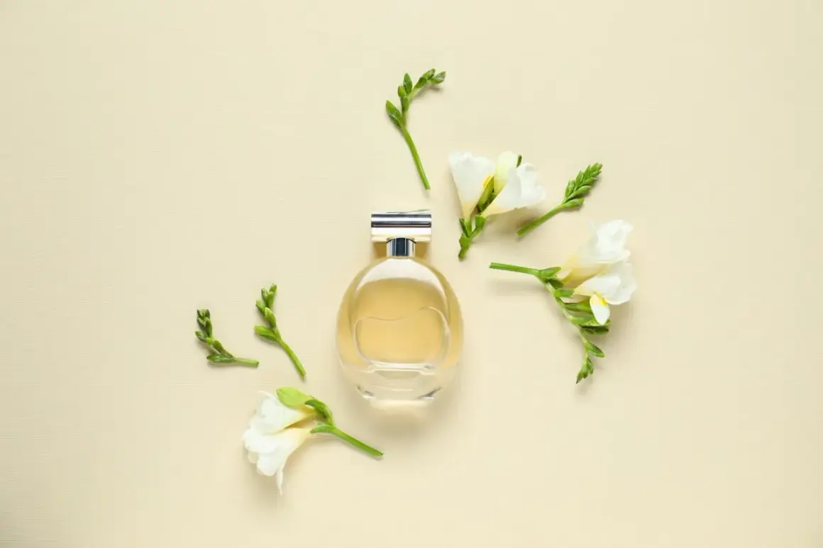 Elegancka butelka perfum otoczona delikatnymi kwiatami frezji. Zapach frezji unosi się w powietrzu, tworząc subtelną kompozycję.