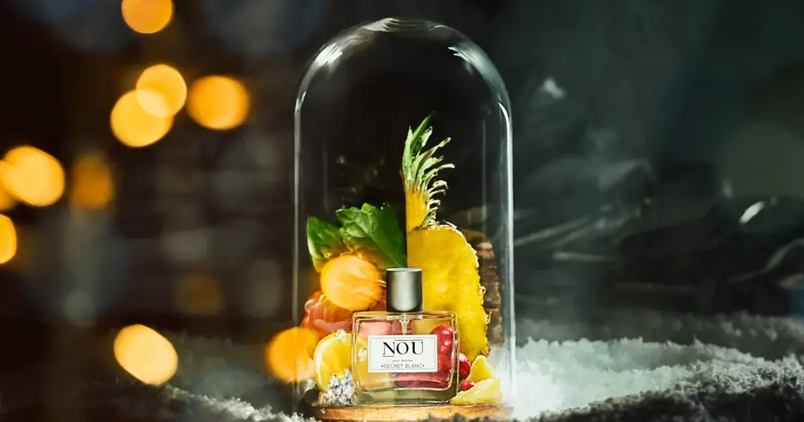 Perfumy NOU "Secret Blanc" w szklanej kopule, otoczone owocami i zielenią. Idealne miejsce, gdzie trzymać perfumy, by zachować ich świeżość.