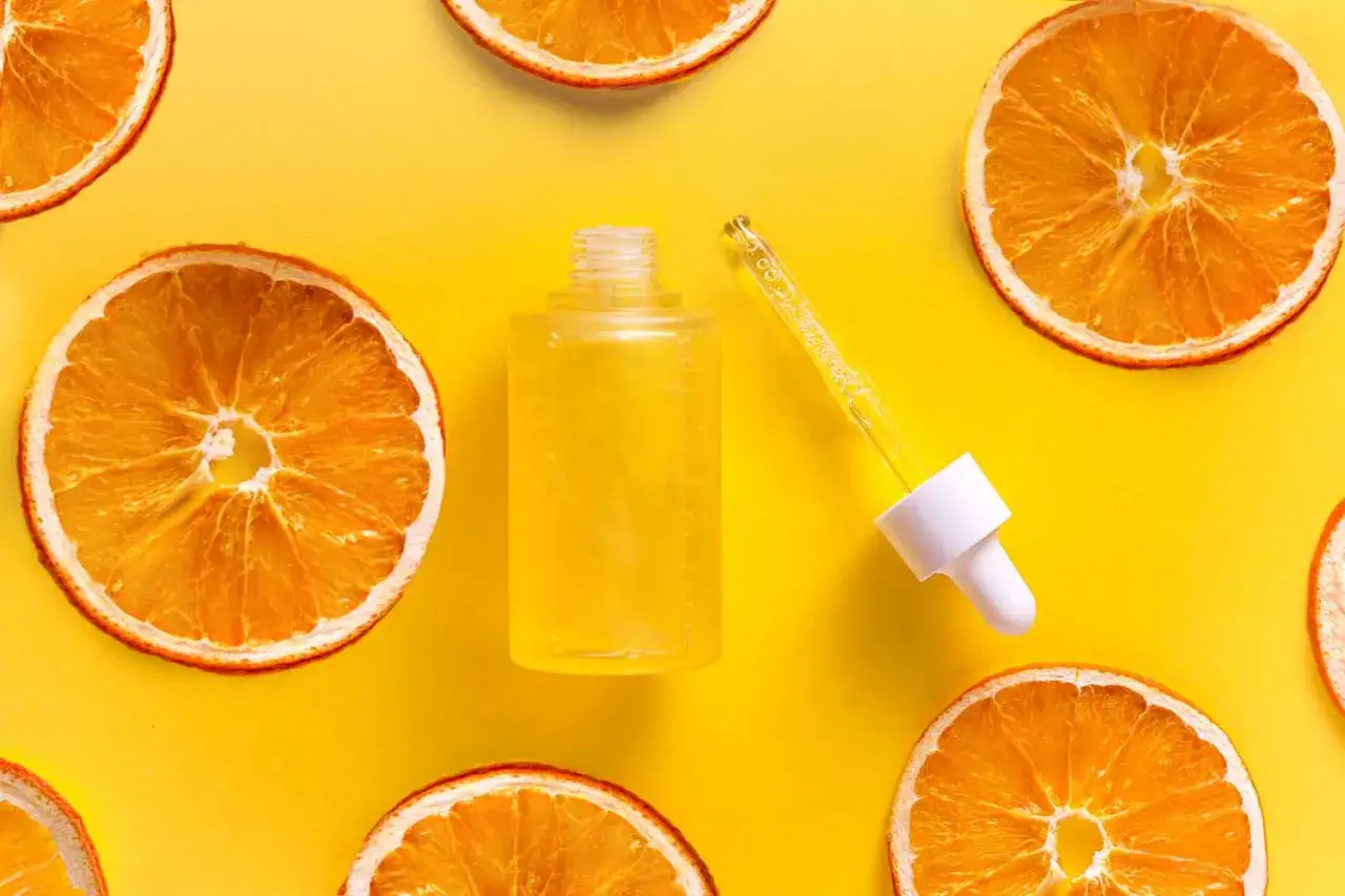 Kwas cytrynowy na twarz w postaci serum z pipetką, otoczony plasterkami suszonej pomarańczy.