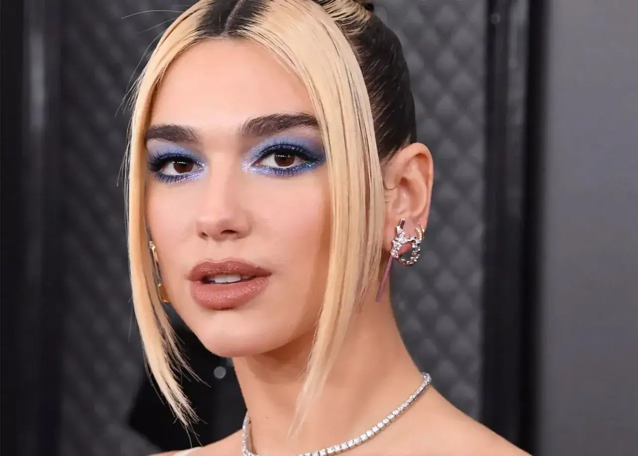 Dua Lipa z olśniewającym makijażem niebieskie cienie, błyszczącą biżuterią i charakterystyczną fryzurą.