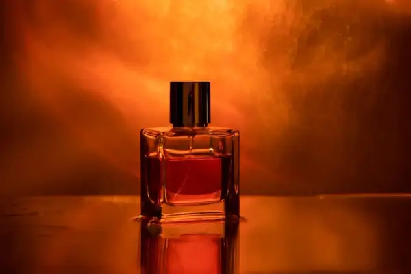 Szklana buteleczka perfum z płynem w odcieniu bursztynu, otoczona ciepłym, świetlistym tłem.