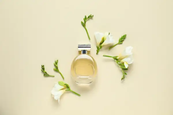Elegancka butelka perfum otoczona delikatnymi kwiatami frezji. Zapach frezji unosi się w powietrzu, tworząc subtelną kompozycję.