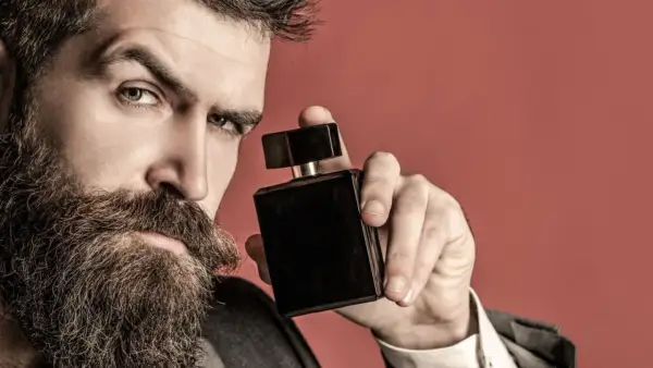Mężczyzna z brodą trzyma czarny flakon perfum. Zastanawia się, gdzie psikac perfumami, by podkreślić swój styl.