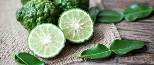 Zielone, pomarszczone owoce i przekrojone na pół limonki, z liśćmi na płótnie. Czuć, jak pachnie bergamotka.