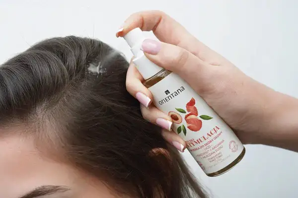 Dłoń aplikuje spray na skórę głowy, by pobudzić skręty włosów. Produkt zawiera liczi i argininę.